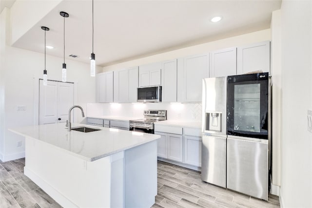 kitchen with white cabinets, light hardwood / wood-style flooring, stainless steel appliances, sink, and an island with sink