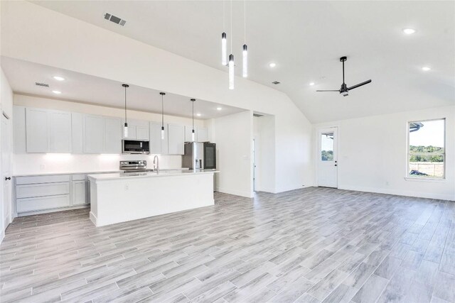 kitchen with a kitchen island with sink, appliances with stainless steel finishes, light hardwood / wood-style flooring, and hanging light fixtures