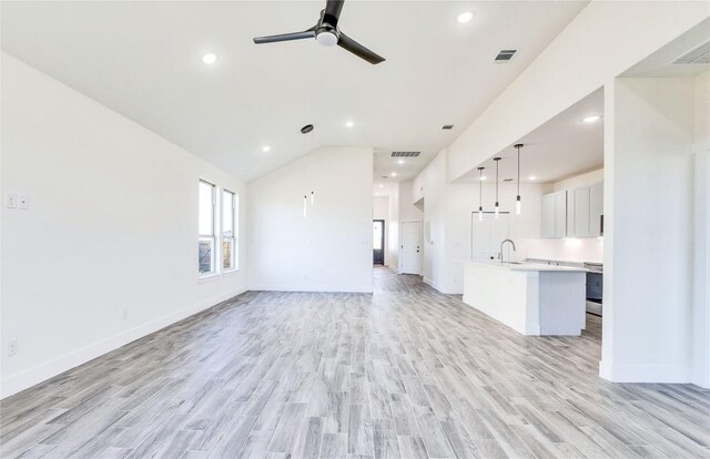 unfurnished living room with vaulted ceiling, light hardwood / wood-style flooring, sink, and ceiling fan