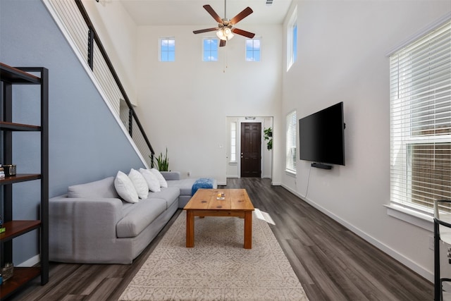 living room with ceiling fan, dark wood-type flooring, a wealth of natural light, and a high ceiling