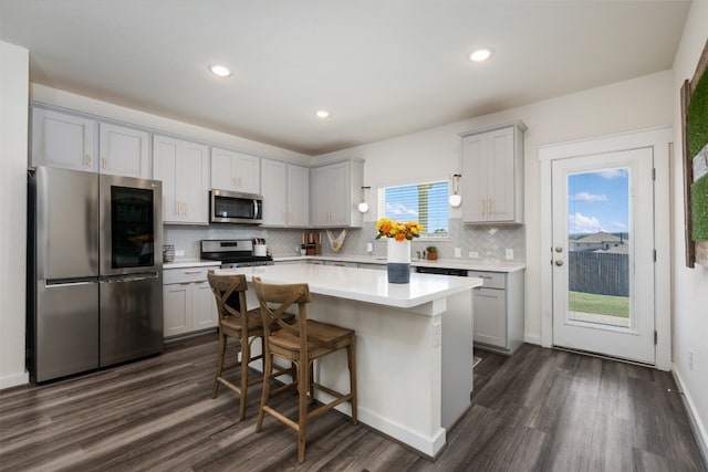 kitchen with tasteful backsplash, dark hardwood / wood-style floors, a kitchen bar, a kitchen island, and appliances with stainless steel finishes