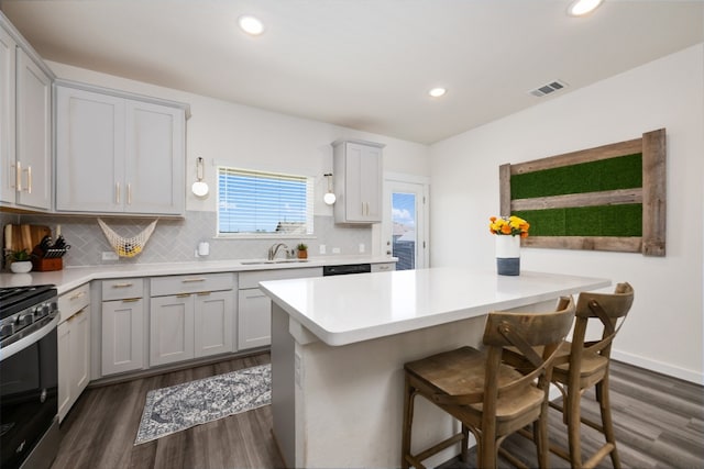 kitchen with a breakfast bar, a center island, backsplash, stainless steel range oven, and dark hardwood / wood-style flooring