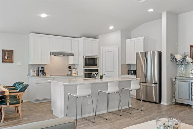 kitchen with a center island with sink, stainless steel appliances, decorative backsplash, white cabinetry, and light wood-type flooring