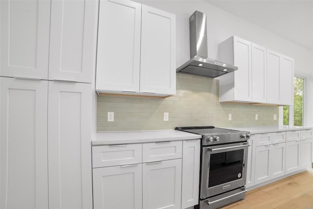 kitchen with white cabinets, light hardwood / wood-style flooring, stainless steel range with electric cooktop, and wall chimney exhaust hood