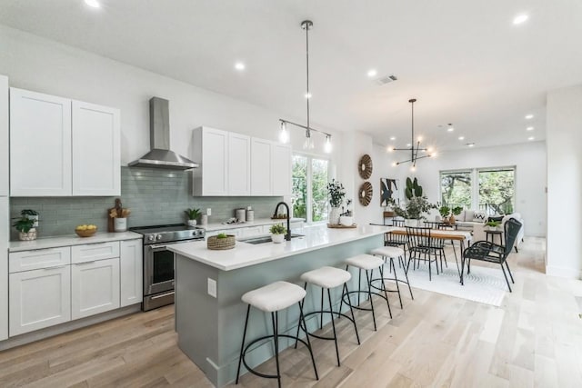 kitchen with an island with sink, white cabinetry, wall chimney exhaust hood, and stainless steel electric range