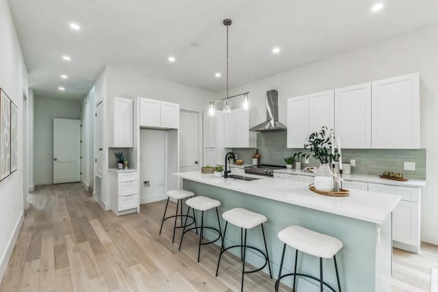 kitchen with sink, wall chimney range hood, pendant lighting, a kitchen island with sink, and white cabinets