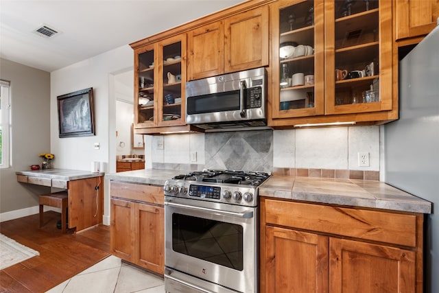 kitchen with light wood-type flooring, stainless steel appliances, and decorative backsplash