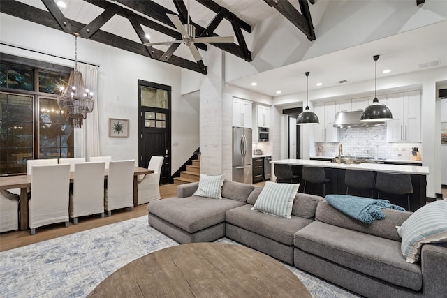 living room featuring high vaulted ceiling, hardwood / wood-style floors, ceiling fan with notable chandelier, and beamed ceiling