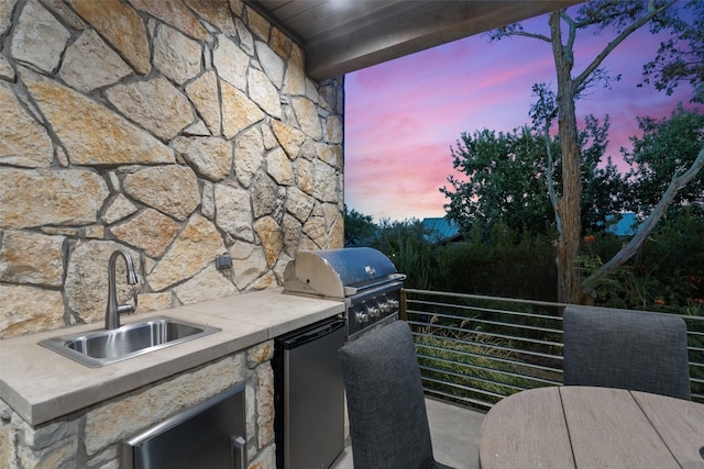 patio terrace at dusk featuring area for grilling, a balcony, and sink