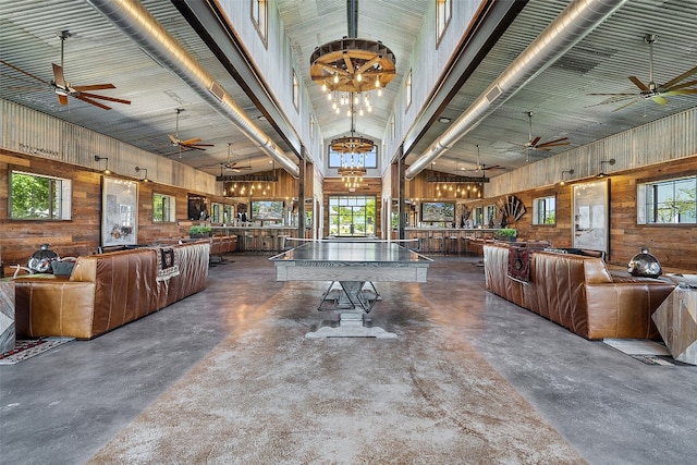 dining room with ceiling fan with notable chandelier, wood walls, high vaulted ceiling, and a healthy amount of sunlight