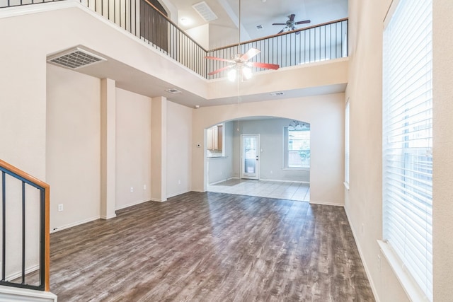 unfurnished living room featuring a high ceiling, ceiling fan, and wood-type flooring