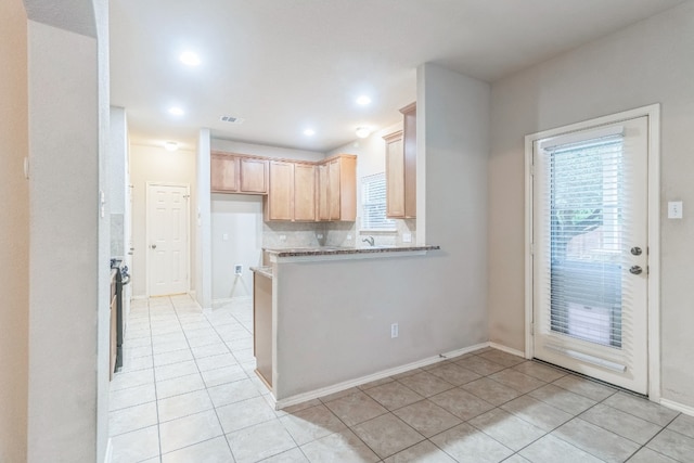 kitchen with light tile patterned floors, light stone counters, light brown cabinets, kitchen peninsula, and tasteful backsplash