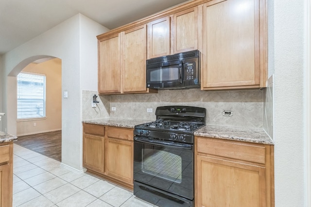 kitchen featuring black appliances, light stone counters, light hardwood / wood-style flooring, and backsplash