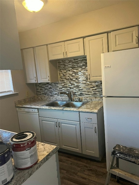 kitchen featuring gray cabinets, a sink, white appliances, tasteful backsplash, and dark wood-style flooring