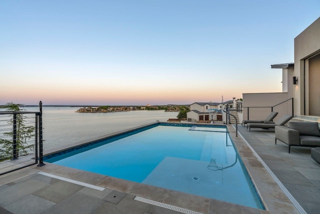 pool at dusk featuring a water view and a patio area