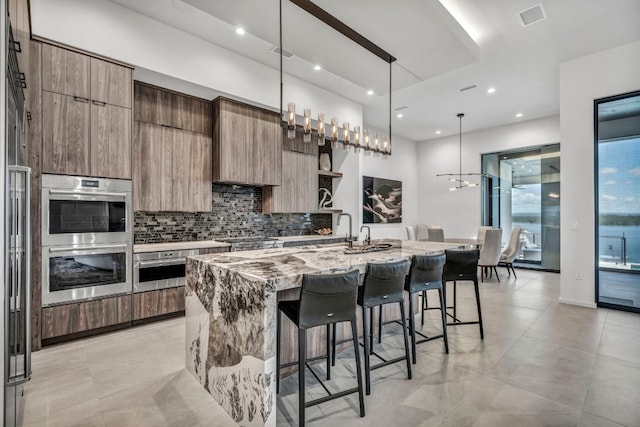 kitchen featuring a center island with sink, pendant lighting, appliances with stainless steel finishes, backsplash, and a breakfast bar