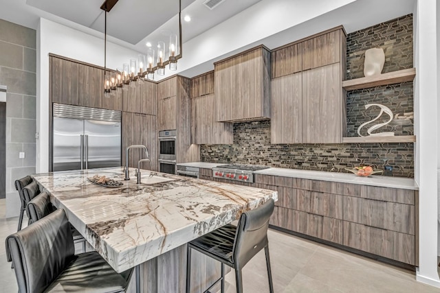 kitchen featuring a kitchen breakfast bar, pendant lighting, appliances with stainless steel finishes, an island with sink, and a chandelier