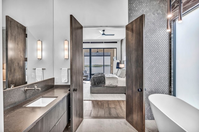 bathroom featuring wood-type flooring, ceiling fan, a tub to relax in, and vanity