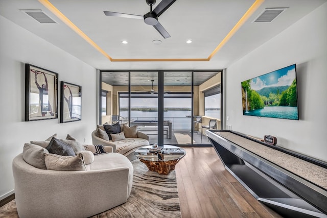 living room featuring a wealth of natural light, ceiling fan, a tray ceiling, and dark hardwood / wood-style flooring