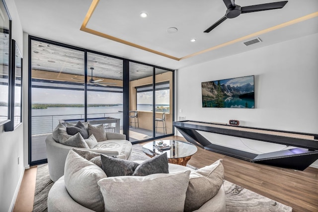 living room with a raised ceiling, hardwood / wood-style flooring, floor to ceiling windows, and ceiling fan