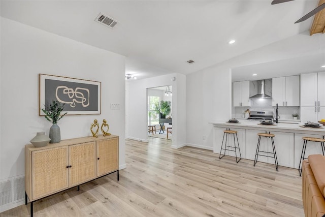 2110 Malvern Hill Dr, Austin, TX 78745 - kitchen with wall chimney range hood, a breakfast bar, stainless steel range, light wood-type flooring, and recessed lighting