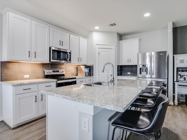 kitchen featuring a center island with sink, light wood-type flooring, appliances with stainless steel finishes, and white cabinets