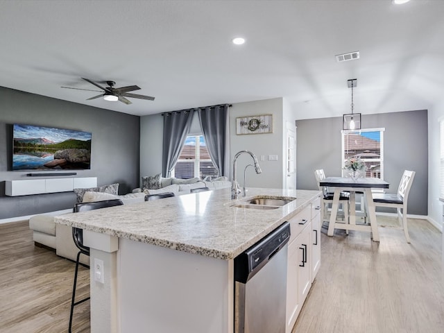 kitchen featuring decorative light fixtures, dishwasher, an island with sink, sink, and white cabinets