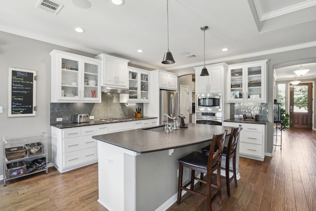 kitchen featuring dark wood-type flooring, white cabinets, stainless steel appliances, and an island with sink