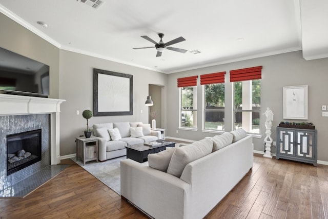 living room with crown molding, ceiling fan, a tiled fireplace, and wood-type flooring