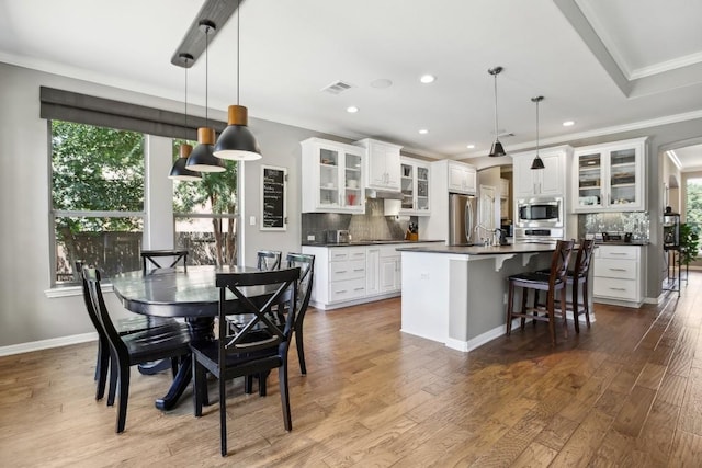 kitchen featuring appliances with stainless steel finishes, dark countertops, ornamental molding, decorative backsplash, and a center island with sink