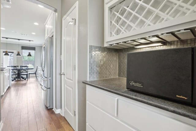 kitchen featuring white cabinets, backsplash, light hardwood / wood-style flooring, stainless steel refrigerator, and pendant lighting