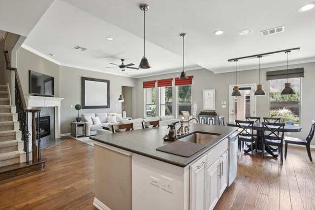 kitchen with a fireplace, a kitchen island with sink, dark hardwood / wood-style flooring, ceiling fan, and white cabinets