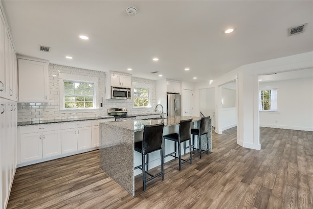 kitchen with dark hardwood / wood-style flooring, light stone countertops, an island with sink, appliances with stainless steel finishes, and white cabinetry