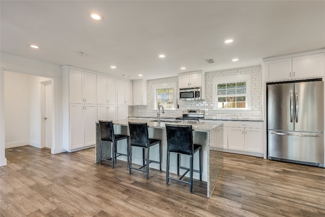 kitchen with stainless steel appliances, an island with sink, light wood-type flooring, and white cabinetry