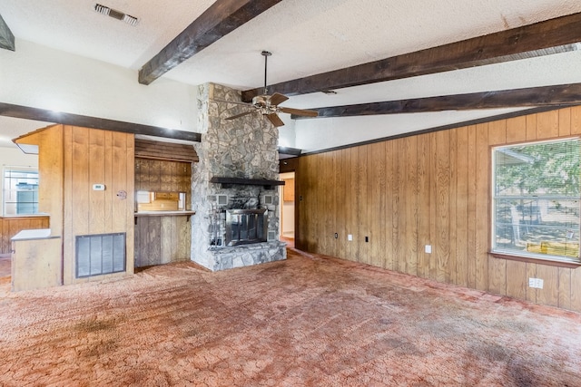 unfurnished living room featuring a stone fireplace, wood walls, a textured ceiling, carpet flooring, and ceiling fan