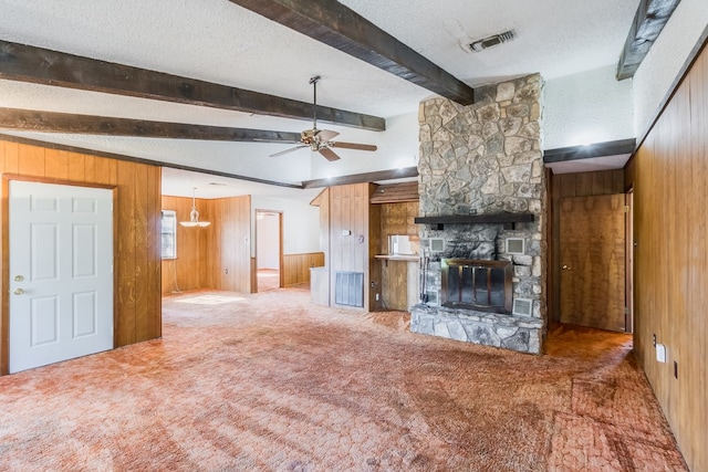 unfurnished living room featuring wooden walls, beam ceiling, ceiling fan, and a stone fireplace