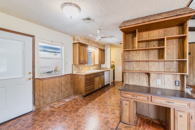 kitchen with dishwasher, a textured ceiling, sink, wood walls, and ceiling fan