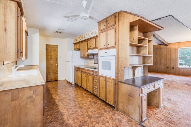 kitchen featuring white appliances, wood walls, a textured ceiling, ceiling fan, and sink