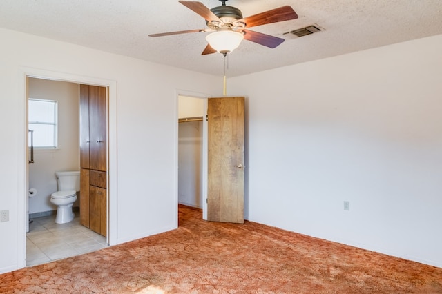 unfurnished bedroom featuring connected bathroom, a textured ceiling, light colored carpet, and ceiling fan