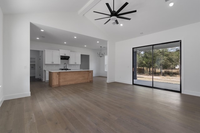 unfurnished living room with sink, ceiling fan with notable chandelier, beamed ceiling, dark wood-type flooring, and high vaulted ceiling