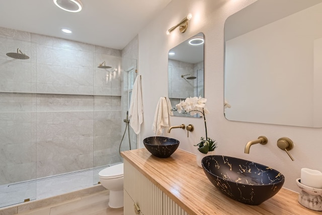 bathroom with vanity, toilet, a tile shower, and wood-type flooring