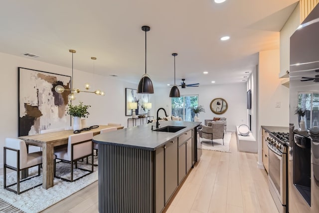 kitchen featuring hanging light fixtures, appliances with stainless steel finishes, ceiling fan with notable chandelier, sink, and an island with sink