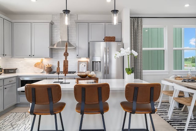 kitchen featuring gray cabinets, appliances with stainless steel finishes, wall chimney exhaust hood, and hanging light fixtures