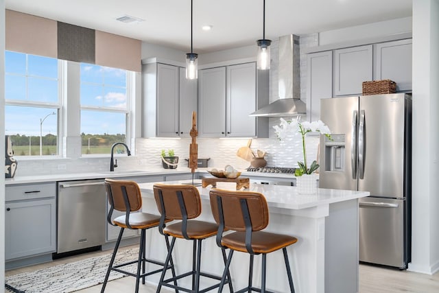 kitchen featuring light wood-type flooring, stainless steel appliances, sink, wall chimney exhaust hood, and a kitchen island