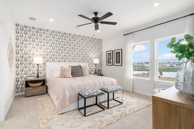 bedroom with ceiling fan, light carpet, and a water view