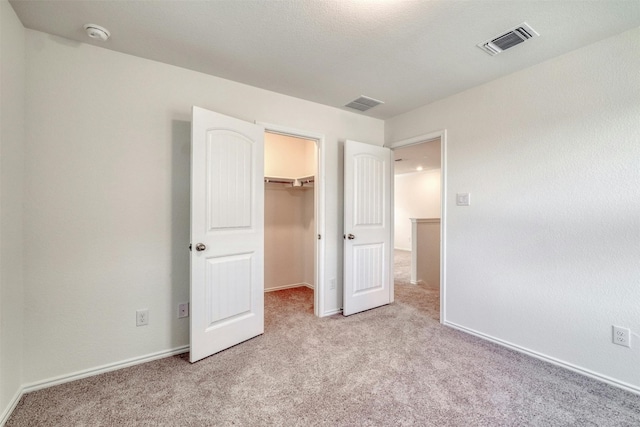 unfurnished bedroom with a walk in closet, light carpet, and a closet