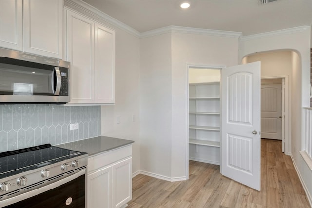 kitchen featuring backsplash, light wood-type flooring, ornamental molding, appliances with stainless steel finishes, and white cabinetry