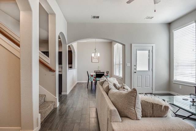 living room with ceiling fan with notable chandelier and dark hardwood / wood-style flooring