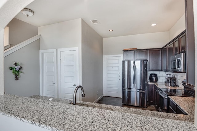 kitchen featuring dark brown cabinets, light stone counters, sink, decorative backsplash, and appliances with stainless steel finishes