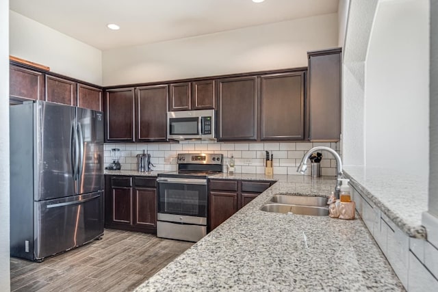 kitchen with tasteful backsplash, stainless steel appliances, light stone counters, sink, and light hardwood / wood-style floors